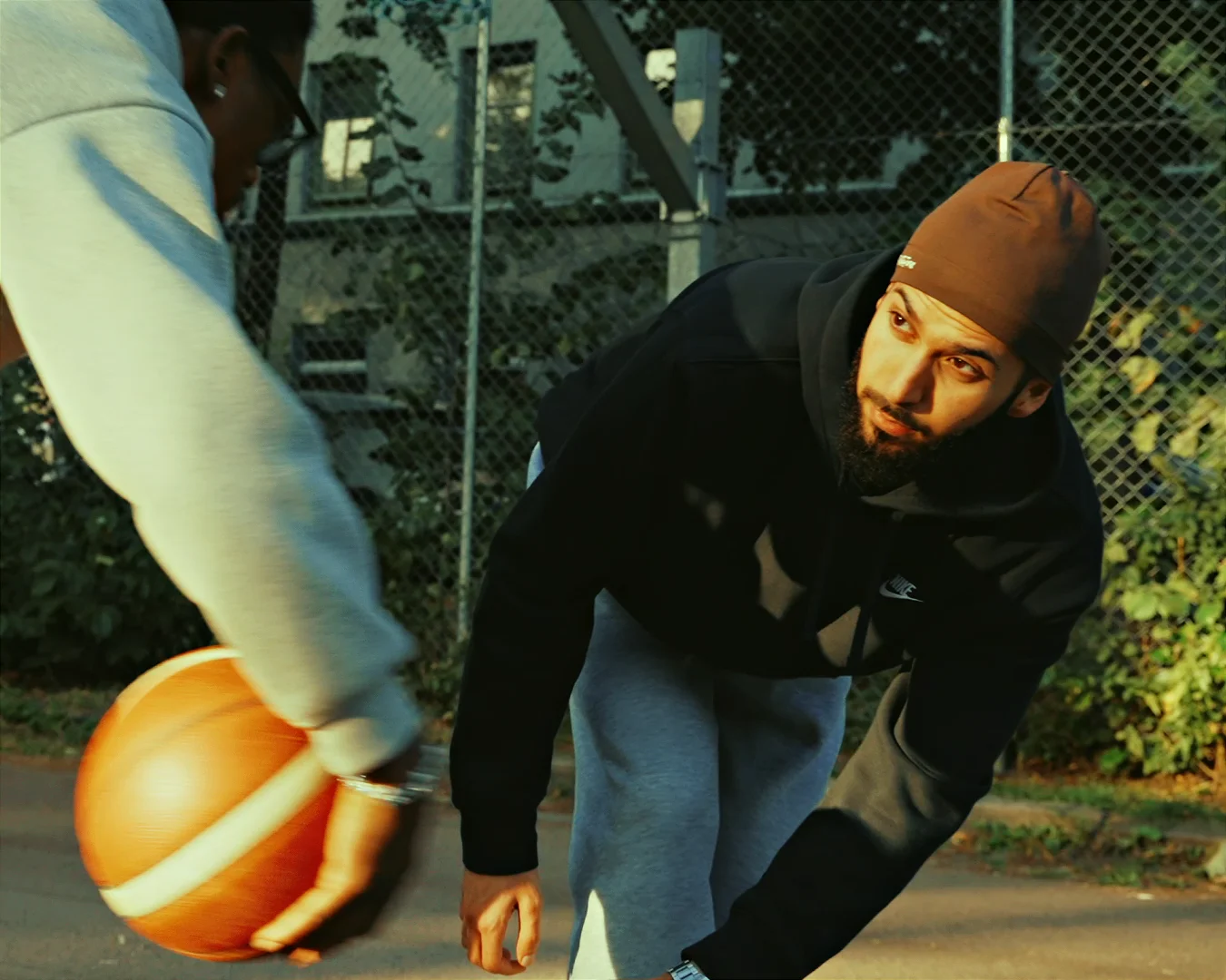 Venner spiller basketball på en utebane i varmt kveldslys.